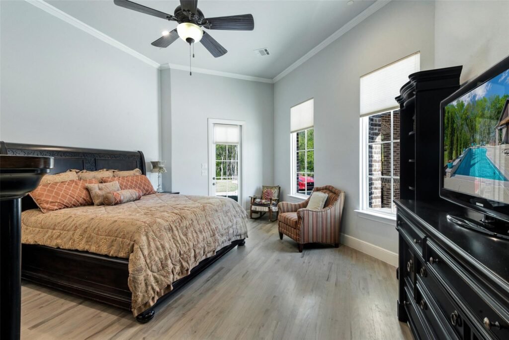 Bedroom with a dark wood bed and beige quilt, light gray walls, and a ceiling fan with a light in the center of the room.