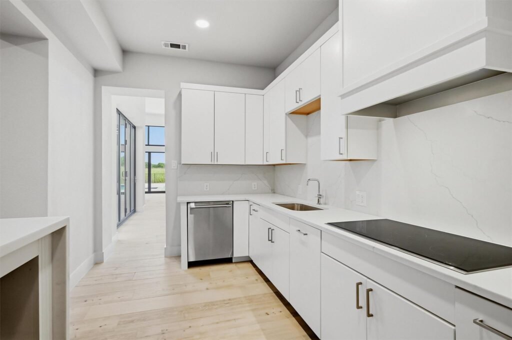 Bright modern kitchen with white cabinets, marble backsplash, and stainless steel appliances.
