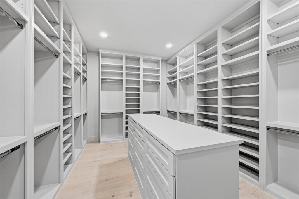 White walk-in closet with floor-to-ceiling open shelves and drawers, empty and well lit by recessed lights