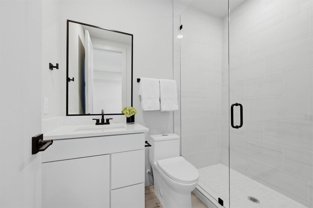 Modern white bathroom with a glass-enclosed shower, white vanity, and black hardware. towels hanging on a rack nearby.