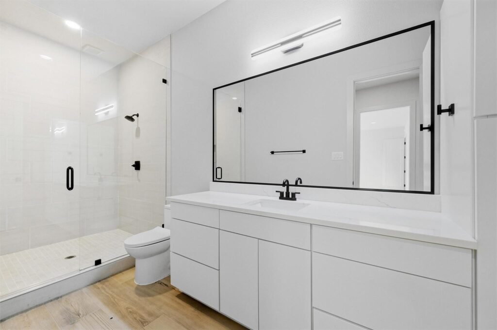 Modern bathroom with a glass-enclosed shower, white vanity, and a large rectangular mirror with black frame and hardware.