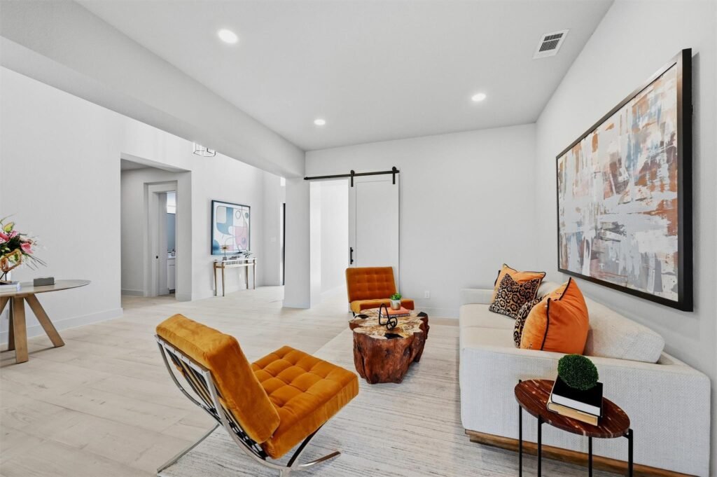 Bright, modern living room with white walls, orange tufted chairs, and a large abstract painting above a white sofa