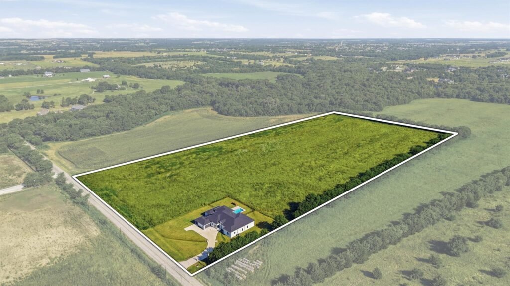 Aerial view of a large rectangular plot outlined in white, with a house at one corner and surrounding fields and trees.
