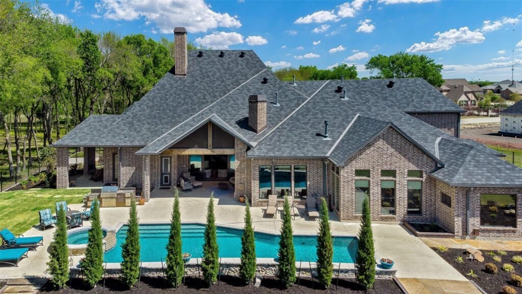 Brick house with multiple gabled roofs, a covered patio, and a rectangular pool surrounded by lounge chairs in a landscaped backyard.