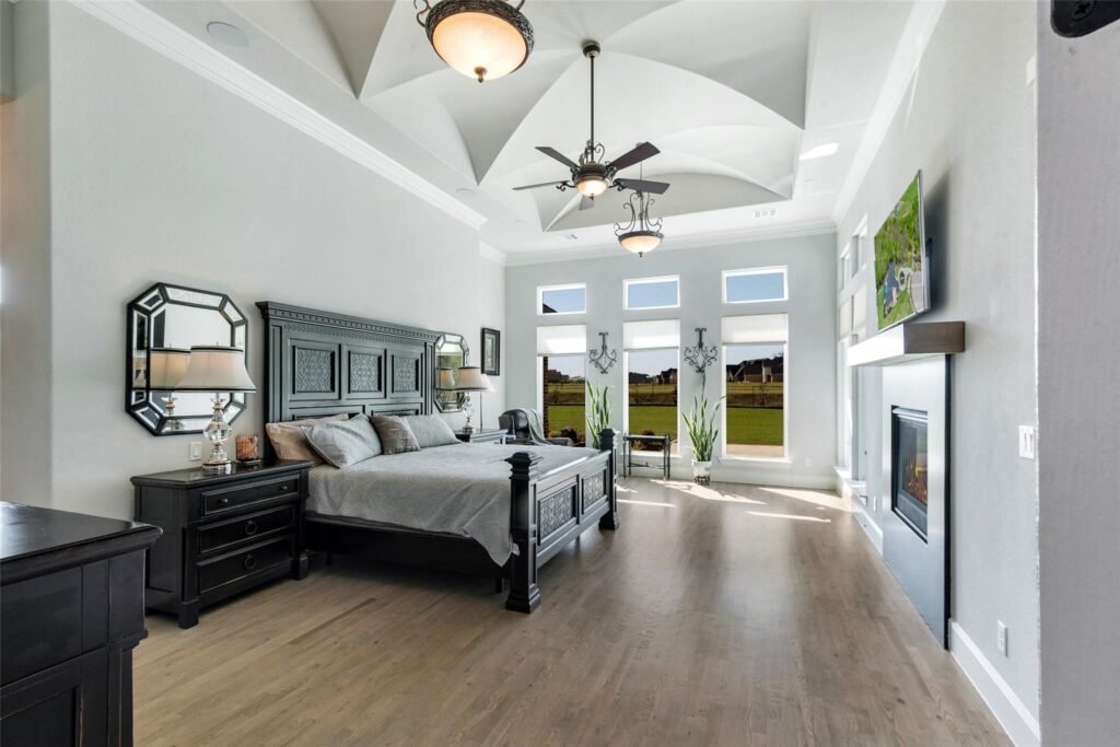 Dark wood king bed with an ornate headboard, matching nightstands, and mirrored accents in a bright modern bedroom; large windows show a green lawn outside.