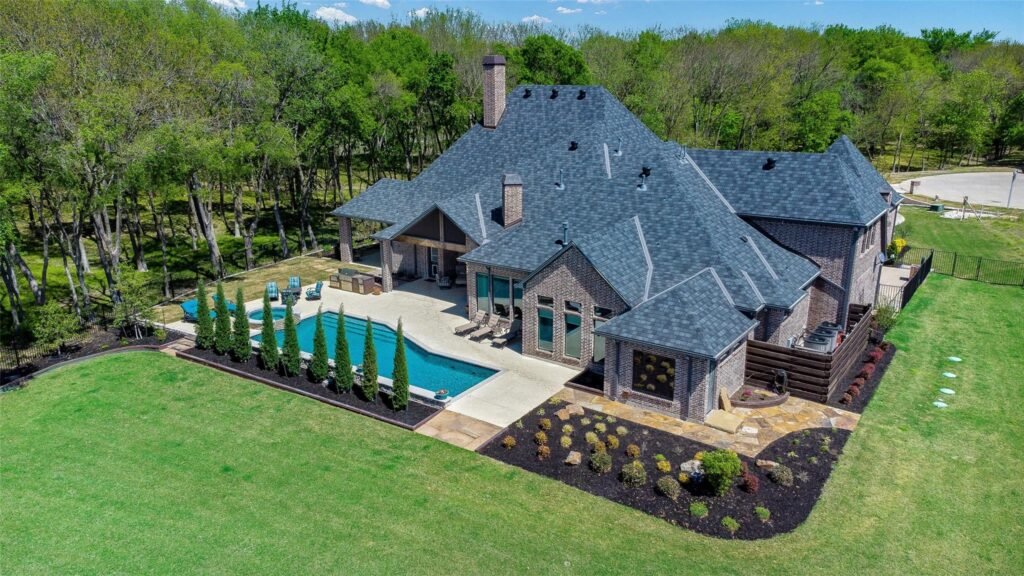 Aerial view of a brick house with a gray slate roof, surrounding lawn, and rectangular backyard pool.