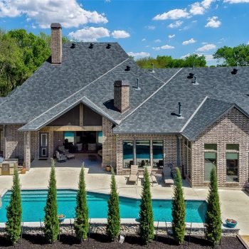 Brick house with multiple gabled roofs, a covered patio, and a rectangular pool surrounded by lounge chairs in a landscaped backyard.